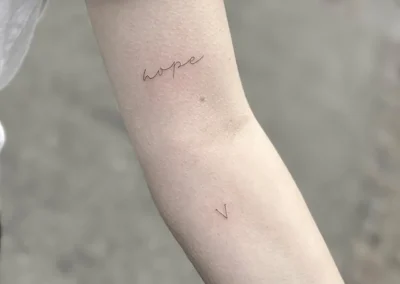 Fineline-tatovering med ordet hope i håndskrift på underarmen