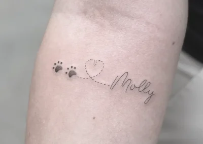 Fineline-tatovering med hundepoter, et hjerte og navnet Molly på underarmen