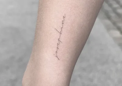 Fineline-tatovering med navnet Josephine i håndskrift på armen