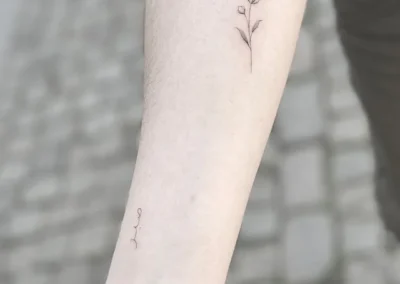 Lille fineline-tatovering af en blomst på underarmen