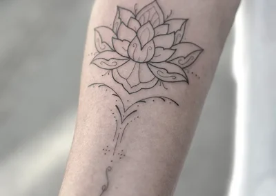 Fineline-tatovering af en lotusblomst med ornamenter på underarmen