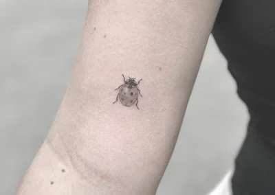 Lille fineline-tatovering af en mariehøne på underarmen