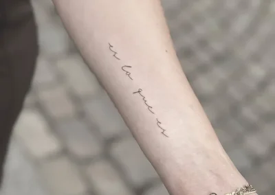 Fineline-tatovering med en håndskrevet sætning langs underarmen