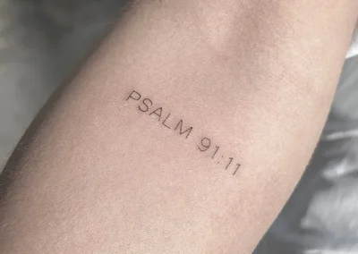 Fineline-tatovering med teksten Psalm 91:11 på underarmen