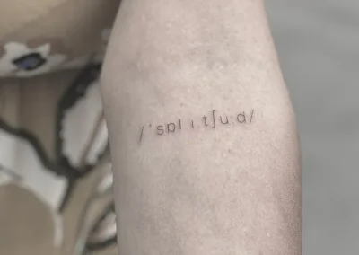 Fineline-tatovering med ordet solitude skrevet i lydskrift på underarmen