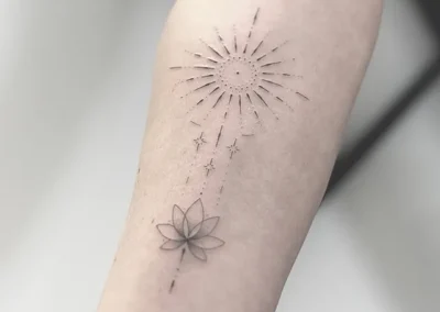 Fineline-tatovering med sol, stjerner og lotusblomst på underarmen