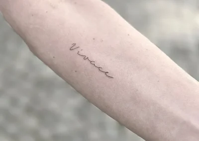 Fineline-tatovering med ordet Vivace i håndskrift på underarmen